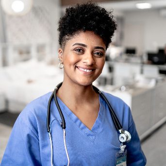 Female doctor wearing blue scrubs facing the camera smiling with a stethoscope around her neck