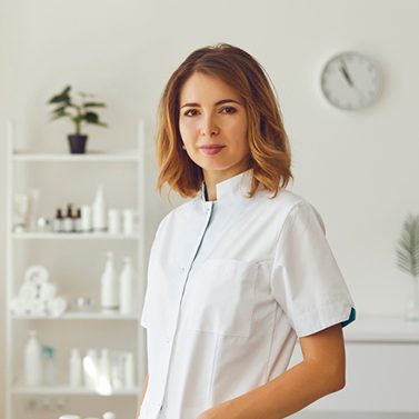 Female doctor wearing white scrubs in a therapy room smiling facing the camera